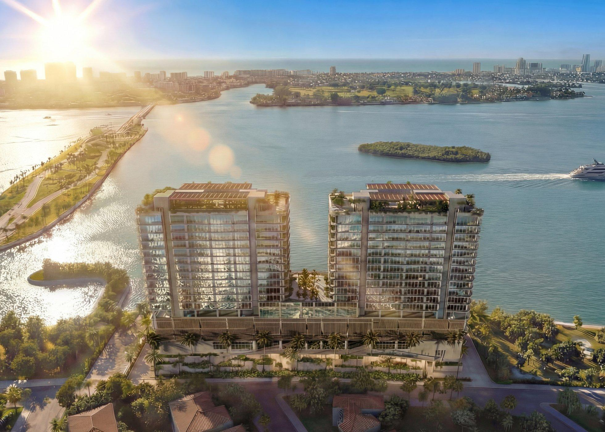 Aerial view of two waterfront residential towers overlooking a wide bay at sunrise.